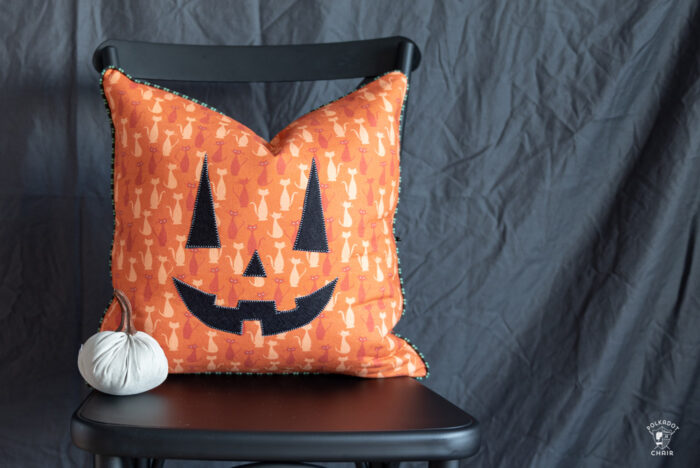 orange pumpkin pillow on black chair in front of gray wall