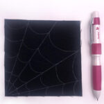 black fabric with a white spiderweb stitched with white thread on white table