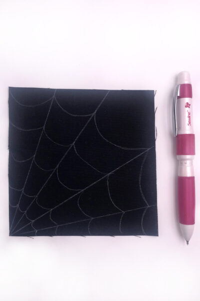 black fabric with a white spiderweb stitched with white thread on white table