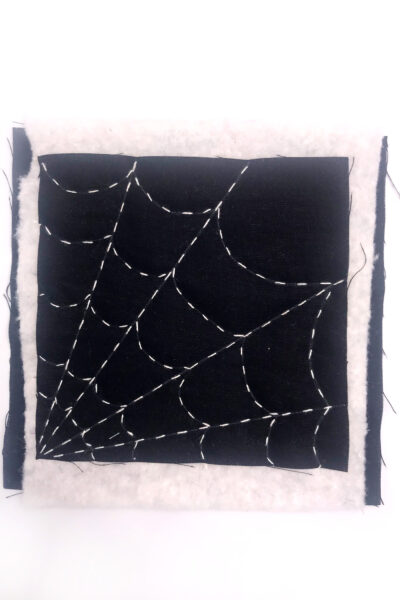 black fabric with a white spiderweb stitched with white thread on white table