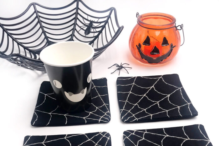 4 black and white spiderweb coasters on white table with halloween props