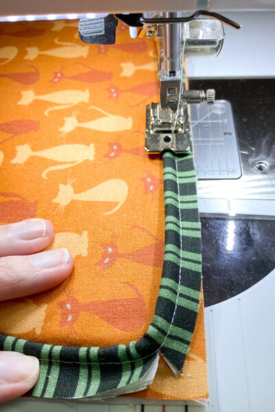 sewing on piping to pillow front. orange pillow with green black piping