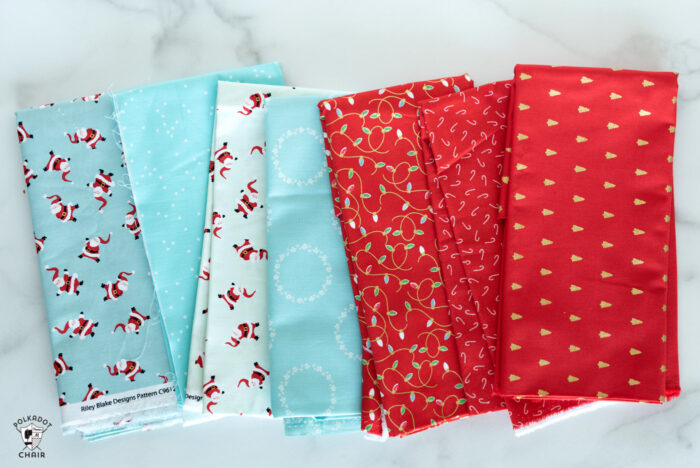 Christmas fabrics in reds and blues in stack on white marble tabletop