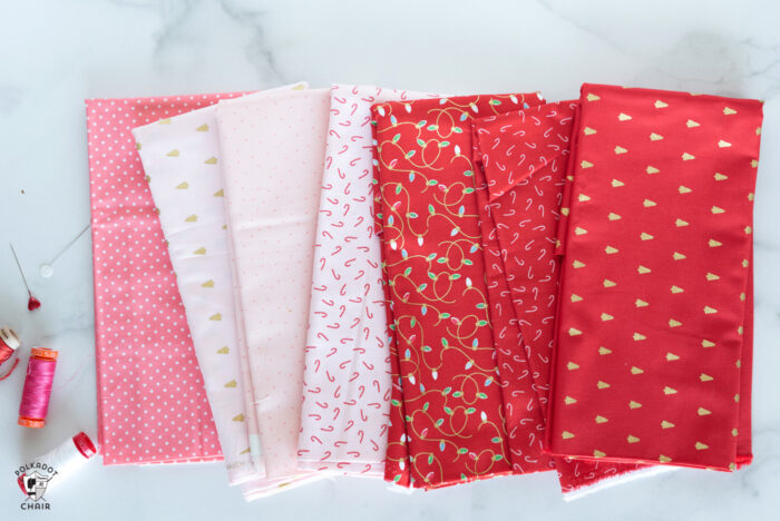 Christmas fabrics in reds and pinks in stack on white marble tabletop