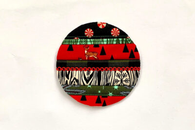 red, green and black christmas ornament in construction with batting on white table