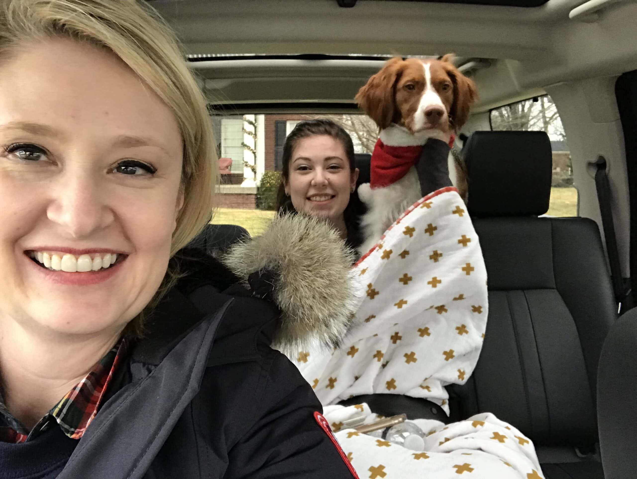 woman in car with girl and dog in background