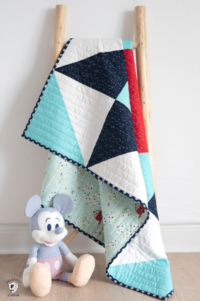 red white and blue baby quilt on white wall with toy in foreground