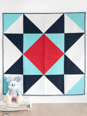 red white and blue baby quilt on white wall with toy in foreground