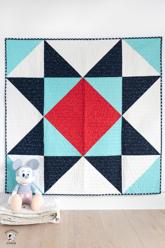 red white and blue baby quilt on white wall with toy in foreground