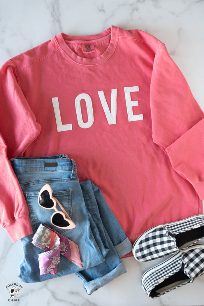 coral love sweatshirt, jeans and shoes on white table