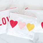 white canvas zip pouches with red lettering and hearts on white tabletop