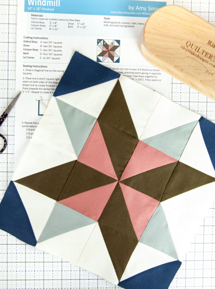 pink, brown and blue quilt block with papers on a white cutting mat