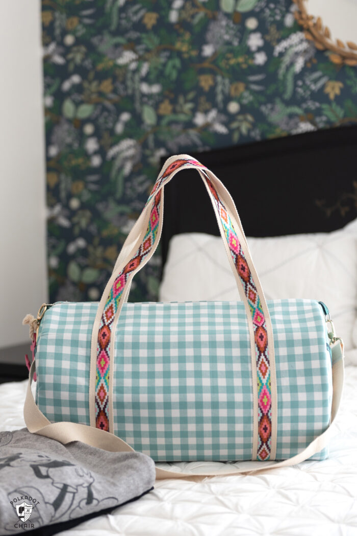 duffle bag on bed with white quilt and black headboard