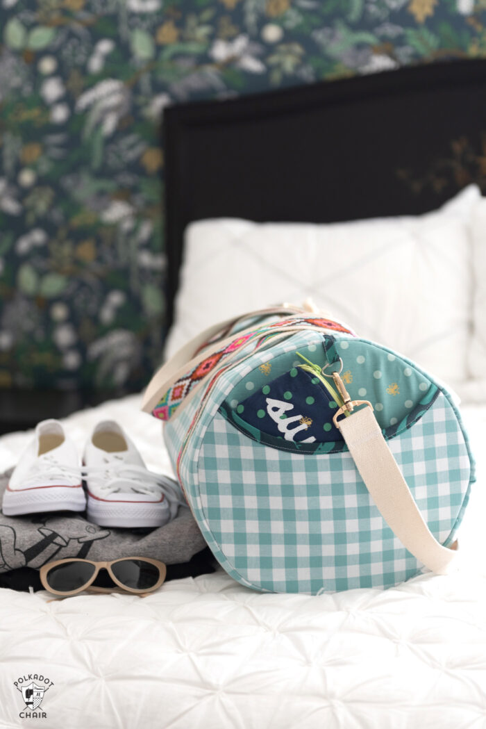 duffle bag on bed with white quilt and black headboard