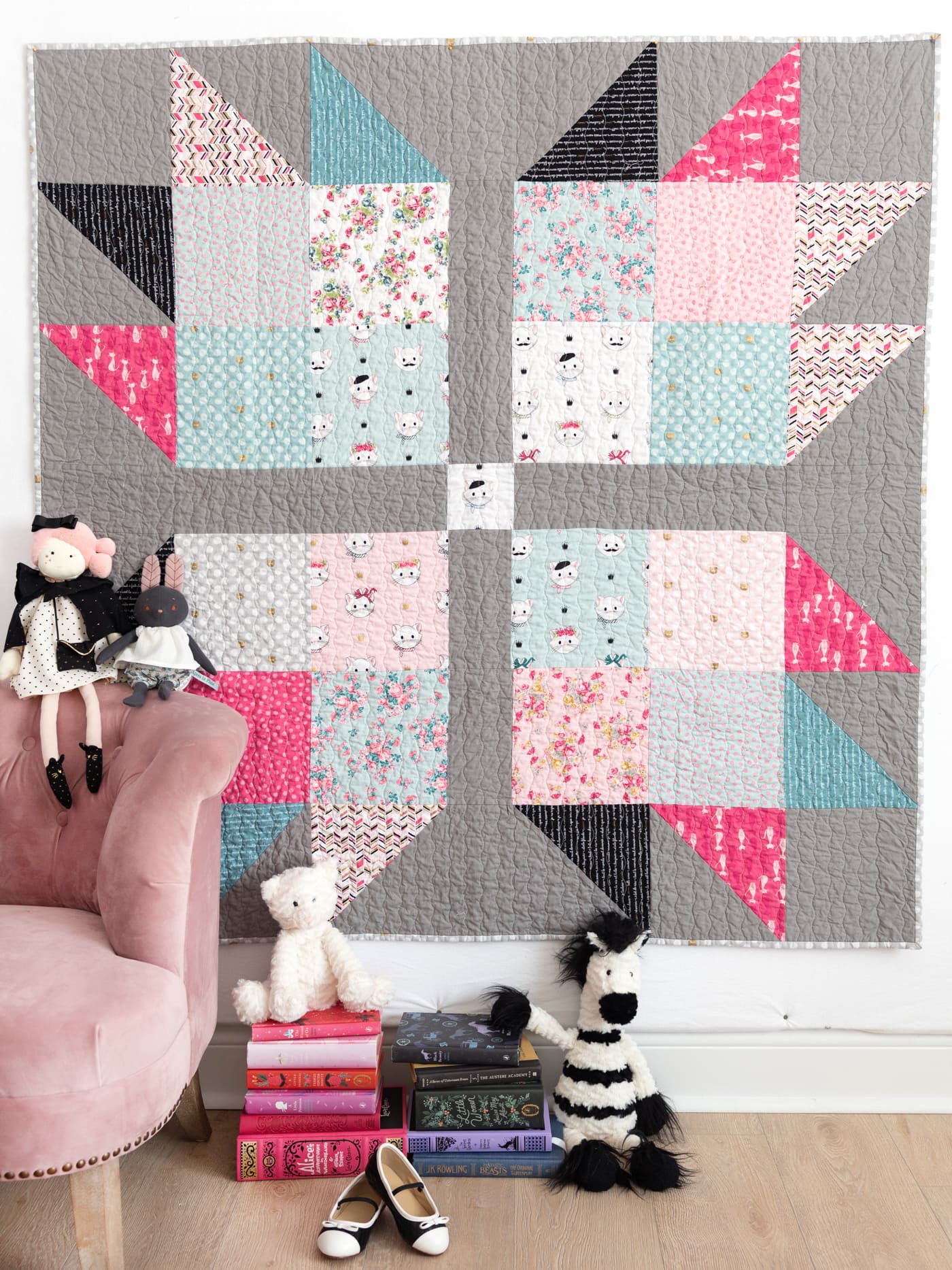 pink, blue and gray quilt on wall with toys