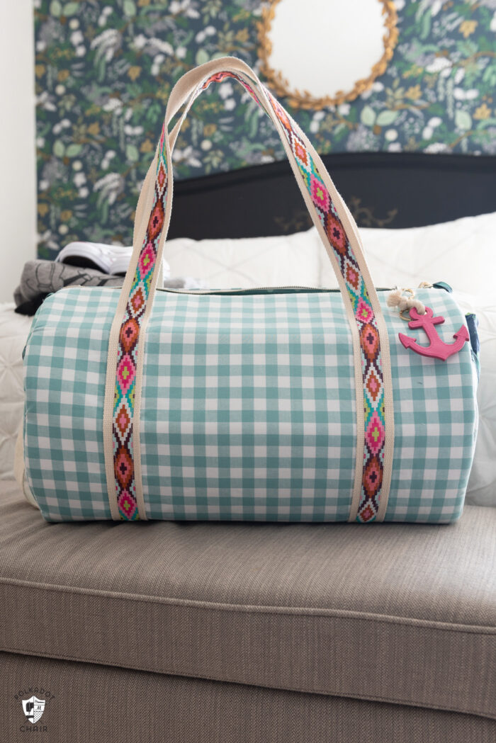 duffle bag on bed with white quilt and black headboard