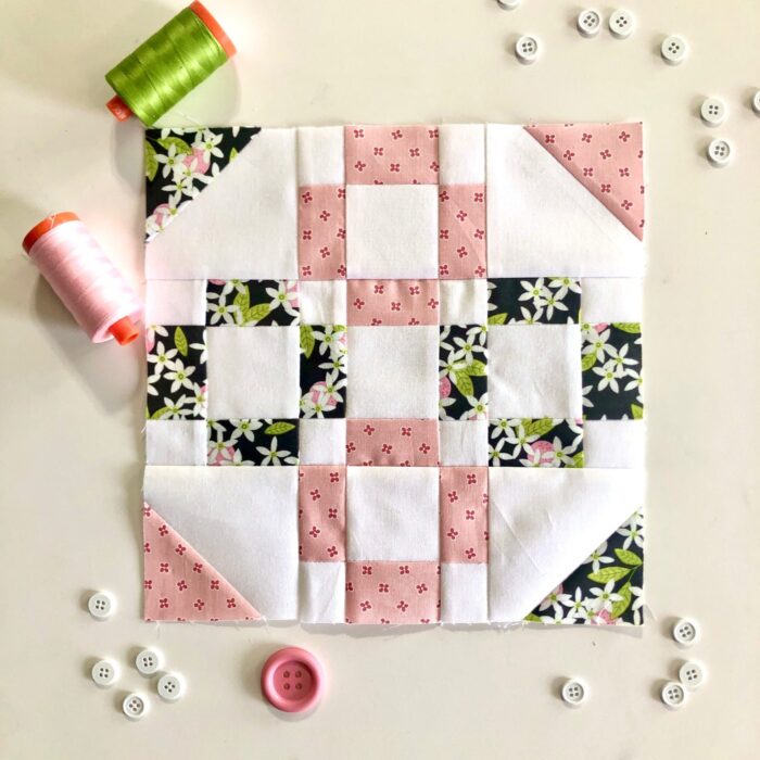 pink and green quilt block on table surrounded by sewing notions