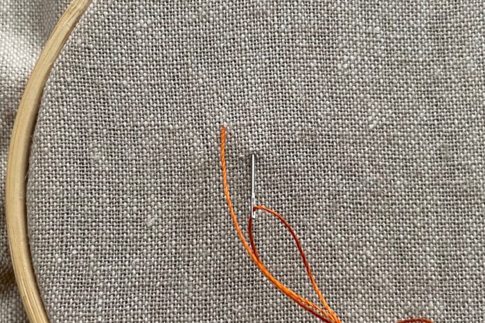 orange embroidery thread on needle on canvas