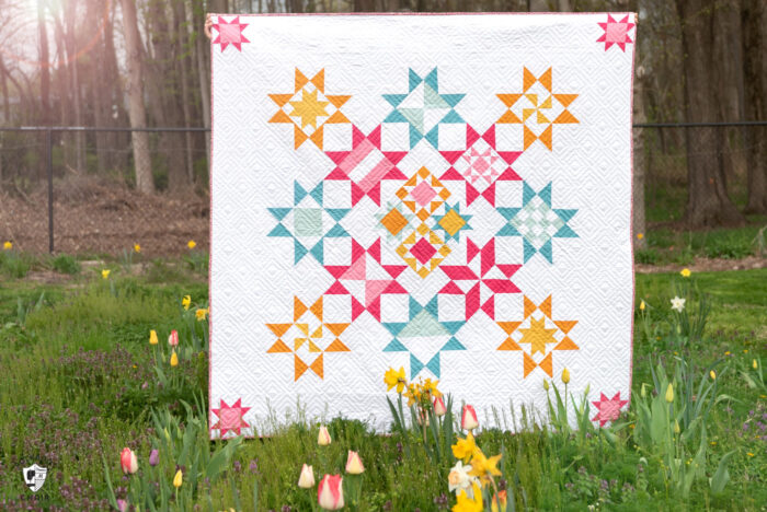 pink, blue and yellow geometric quilt in field of flowers