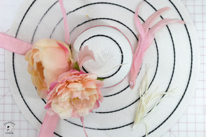 White hat with black stripes with flowers, feathers and ribbons on white cutting table