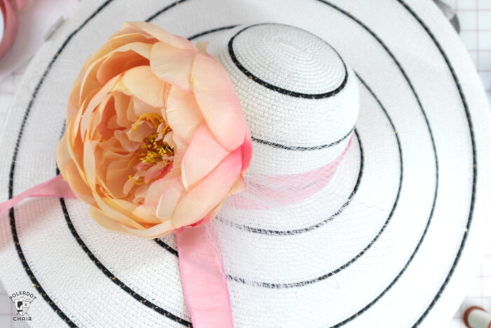 White hat with black stripes with flowers, feathers and ribbons on white cutting table