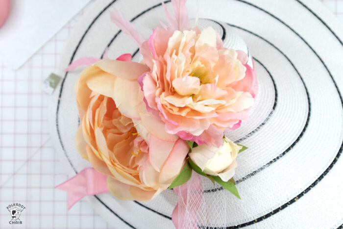 White hat with black stripes with flowers, feathers and ribbons on white cutting table