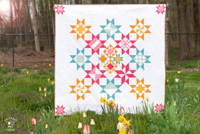 pink, blue and yellow geometric quilt in field of flowers