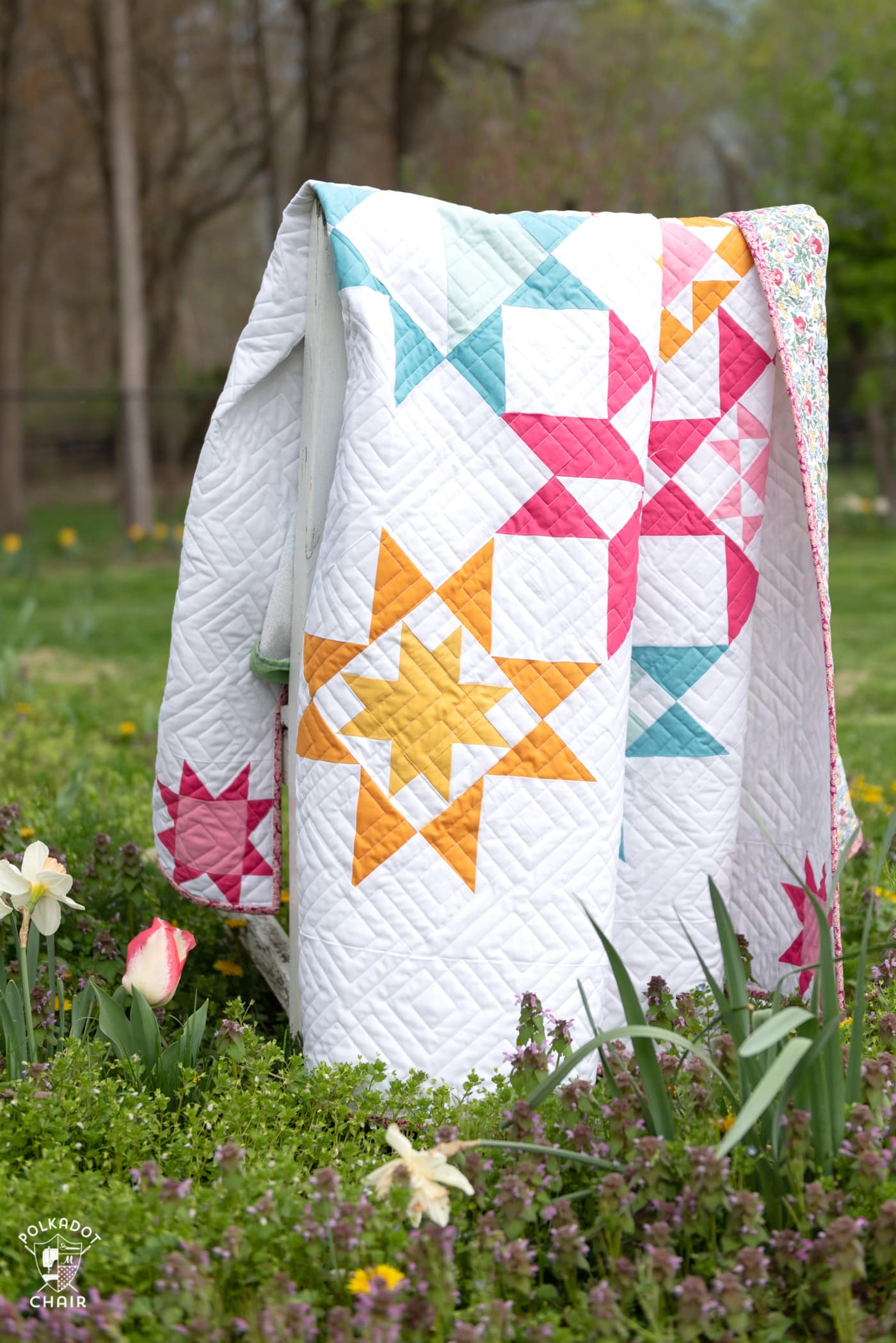 pink, blue and yellow geometric quilt in field of flowers