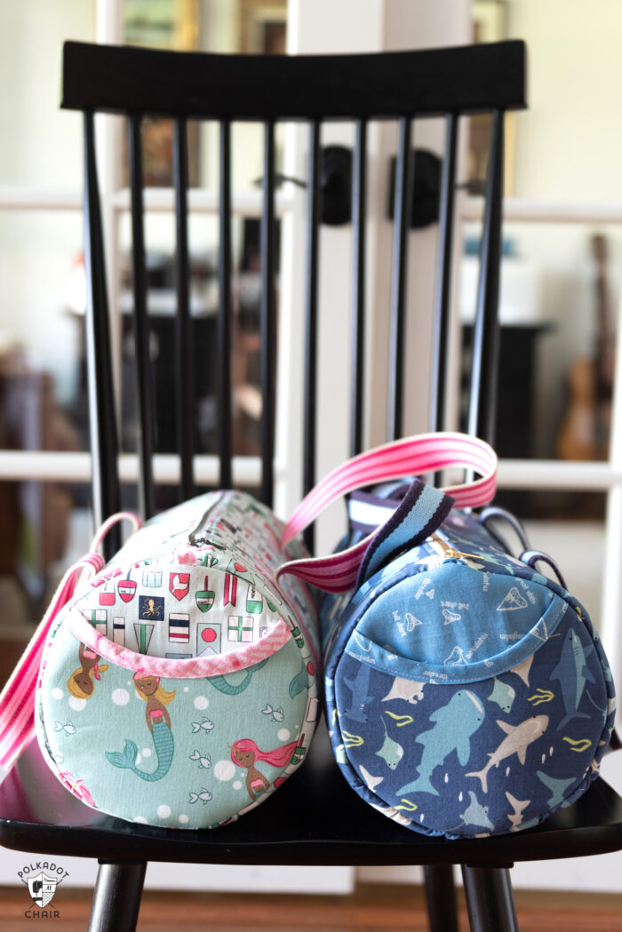 two duffle bags in aqua and blue sitting on chair in front of french doors