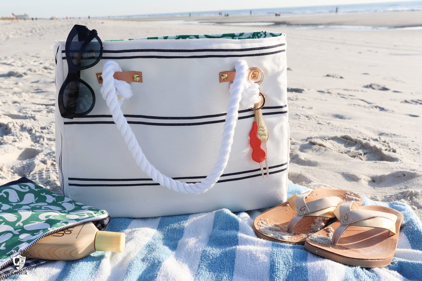 white and blue striped bag on beach with towel and shoes