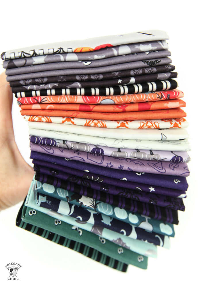 hand holding a stack of halloween fabrics in gray, orange, ivory and green