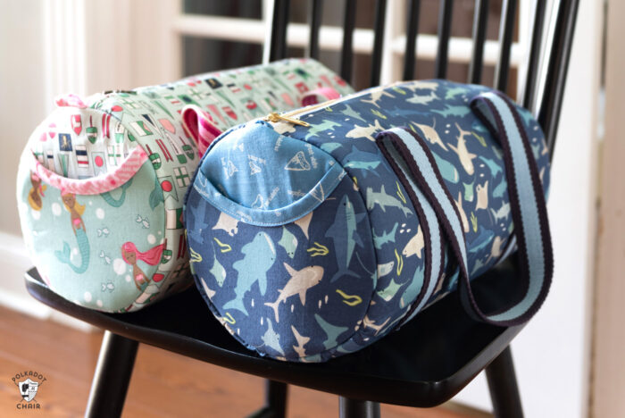 two duffle bags in aqua and blue sitting on chair in front of french doors