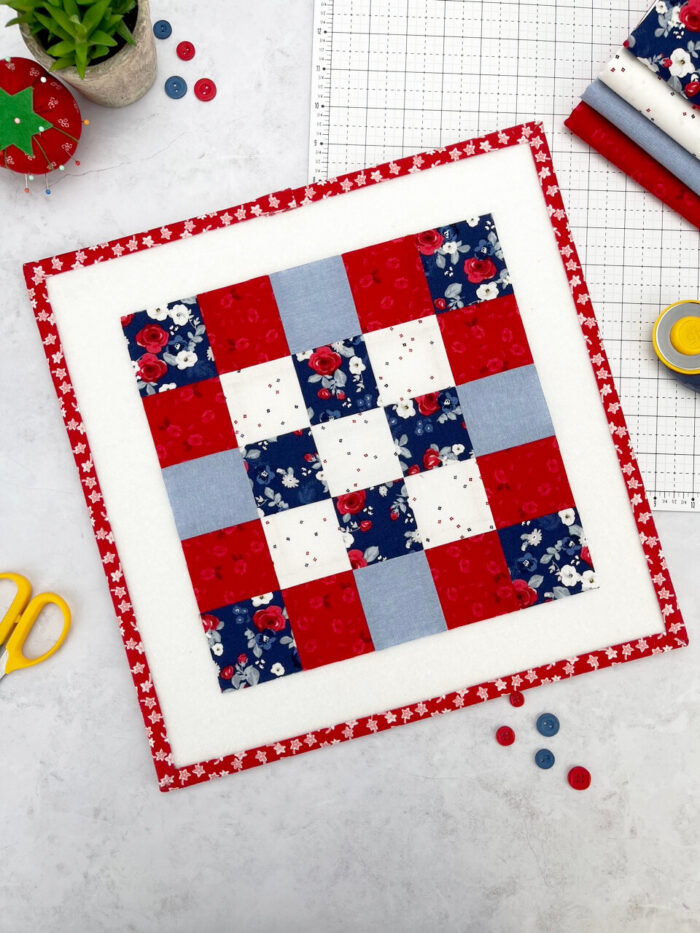 red white and blue quilt block on white cutting mat with buttons and scissors