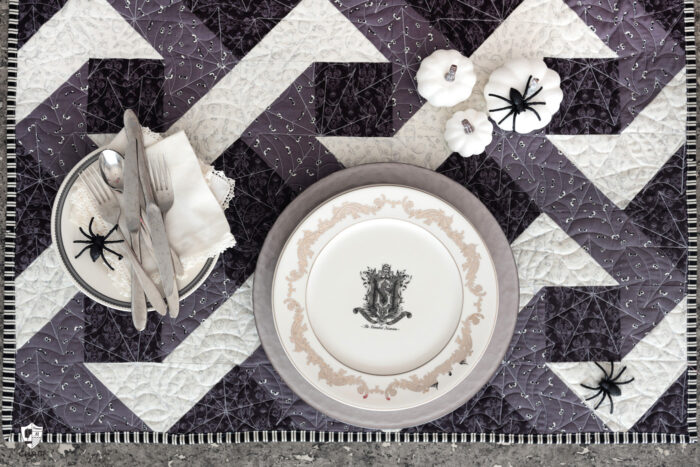 Halloween table setting with gray and black quilted table topper and white plates