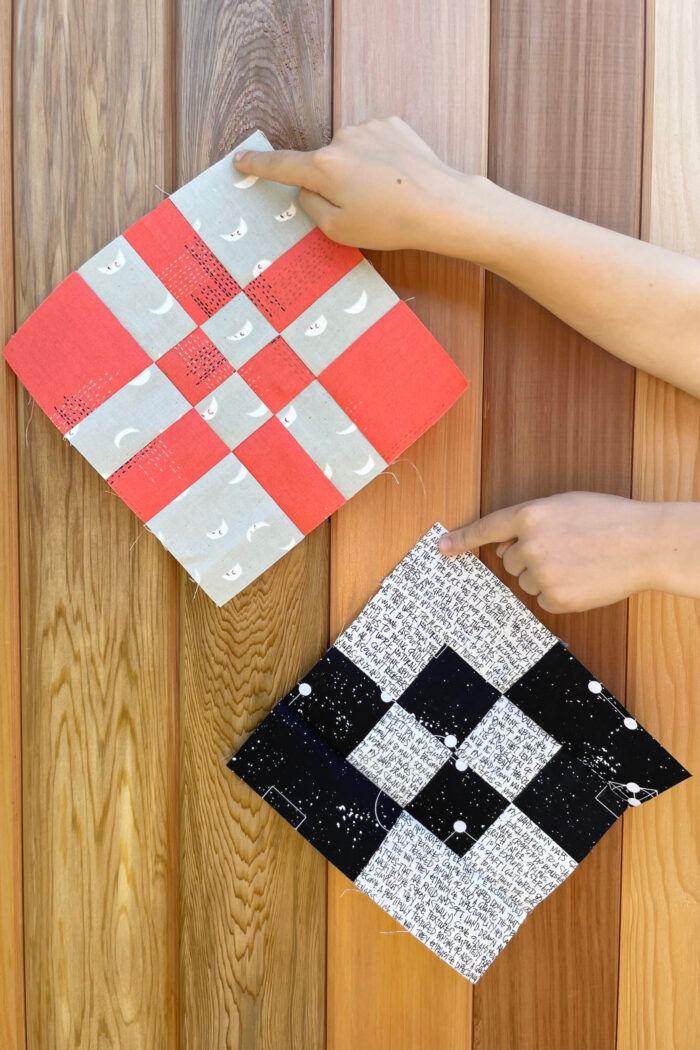 hands holding two quilt blocks in front of wood fence