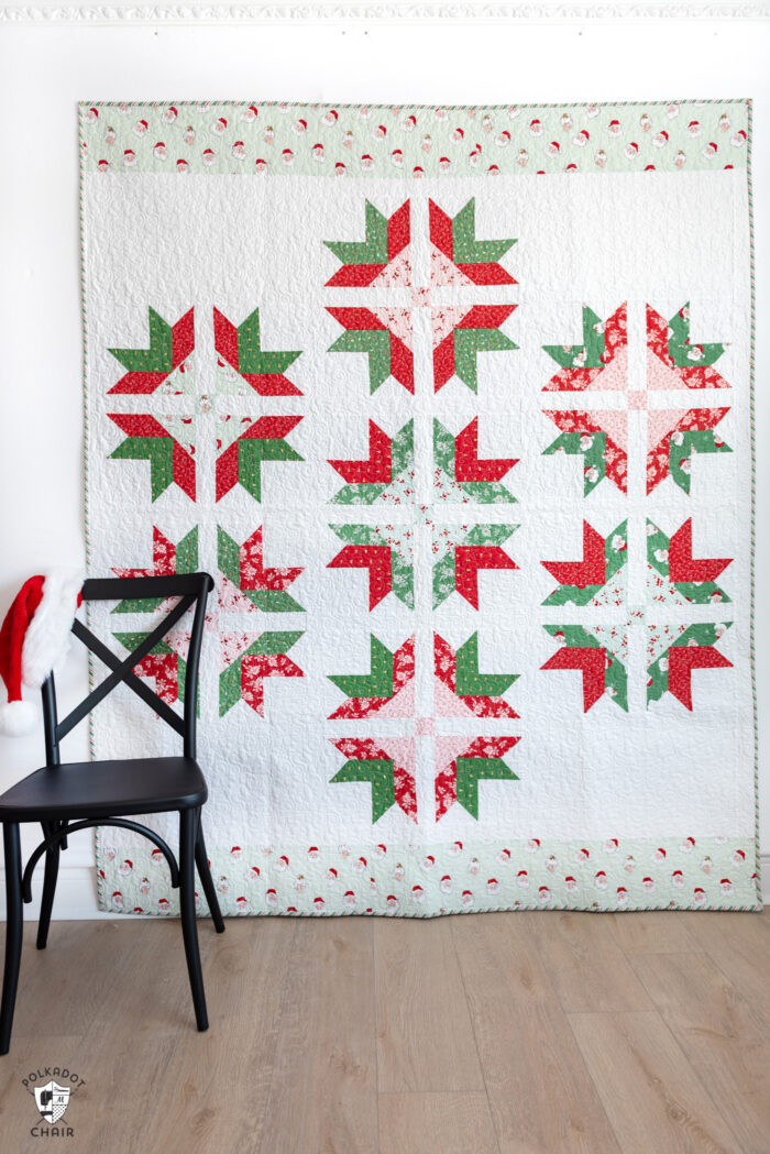 pink, red, green graphic quilt on white wall with black chair in foregroud.