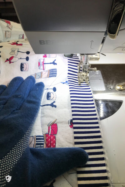 gloved hand holding a quilt under a sewing machine