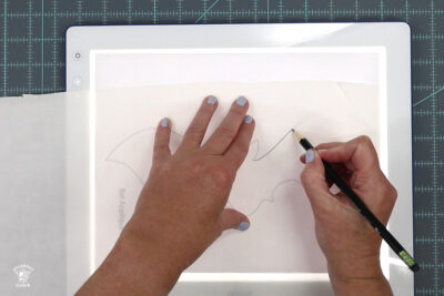 hands tracing a bat shape on light box