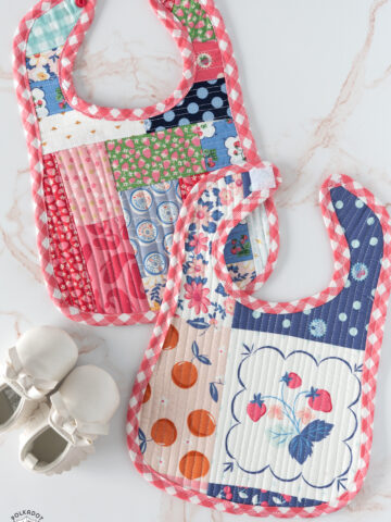 colorful scrappy baby bib on white marble tabletop with shoes