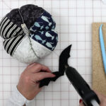 hands constructing fabric pumpkin with tools on white cutting mat