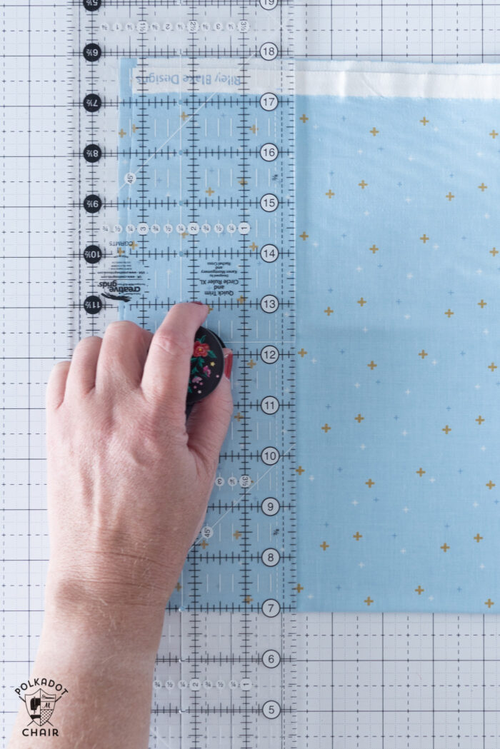 hand on quilt ruler on cutting mat with blue fabric