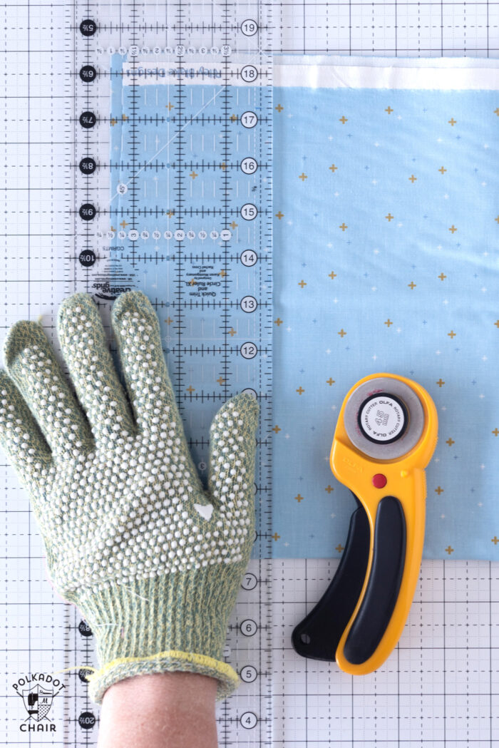 hand with cut glove on white cutting mat with quilt ruler and rotary cutter