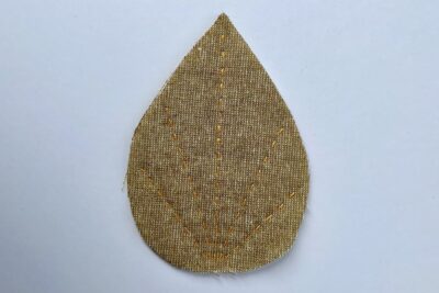 brown fabric leaf with needle and thread on white table