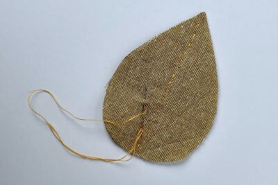 brown fabric leaf with needle and thread on white table