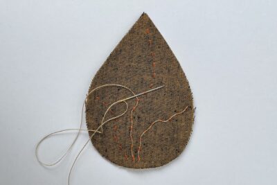 brown fabric leaf with needle and thread on white table