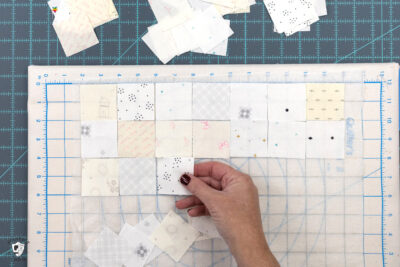 cream and white squares of fabric laid out on portable cutting board