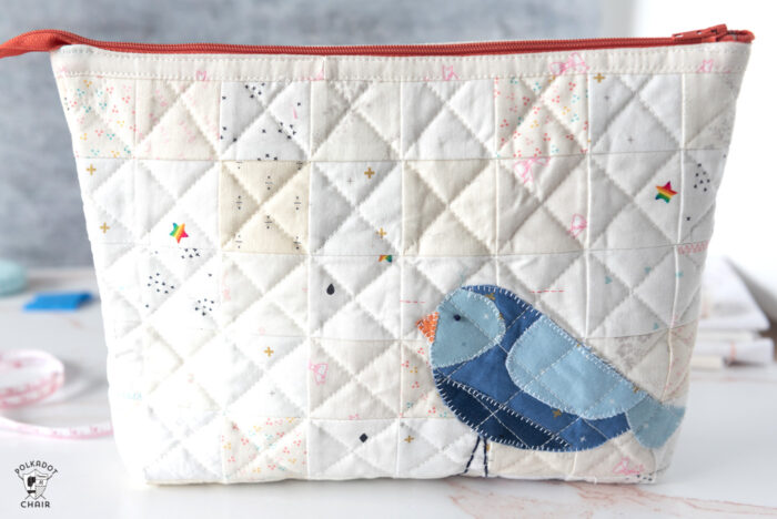 Ivory quilted zip pouch with blue bird on white countertop