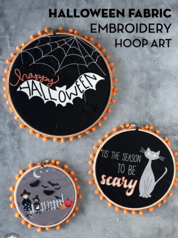 3 black fabric embroidery hoops on gray table with orange pom pom trim