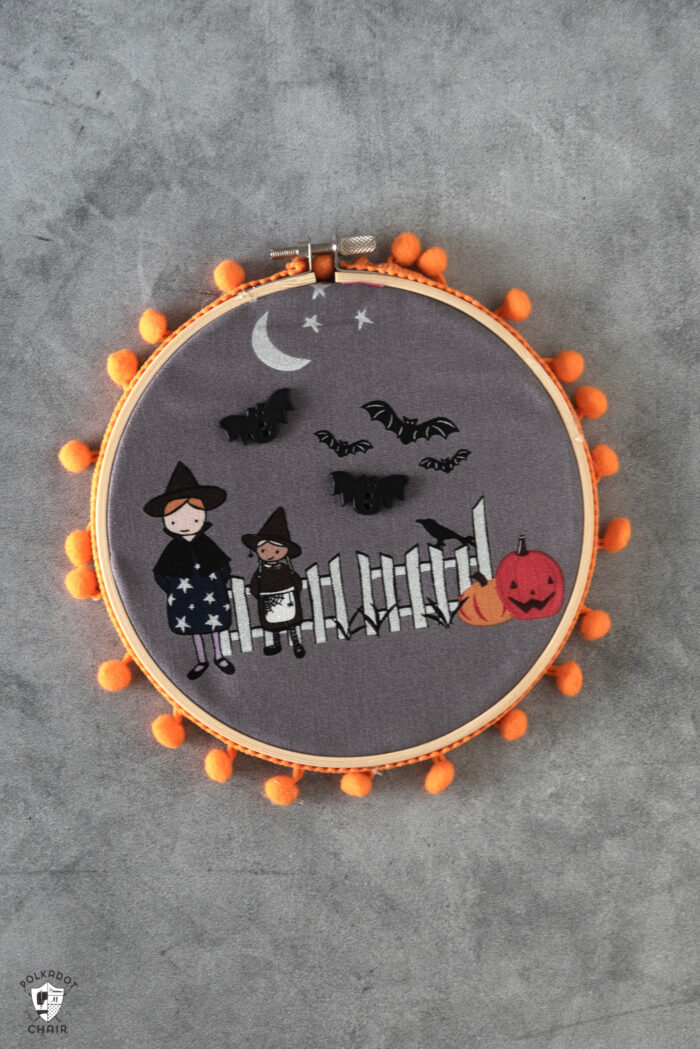 black fabric embroidery hoops on gray table with orange pom pom trim