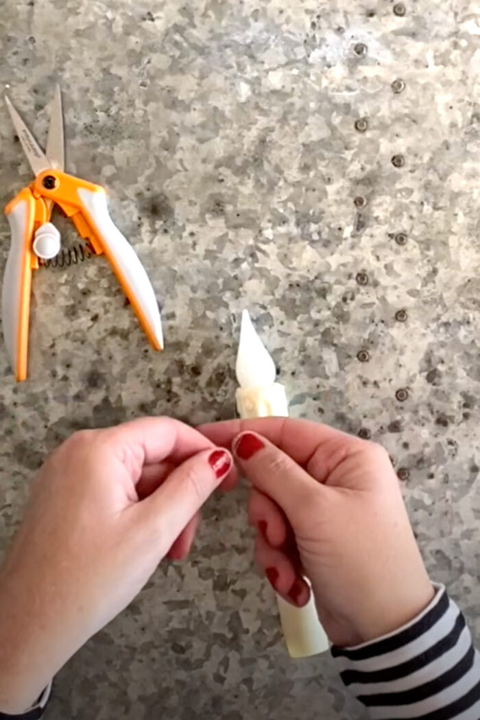 hands tying fishing line to a candle on top of metal table